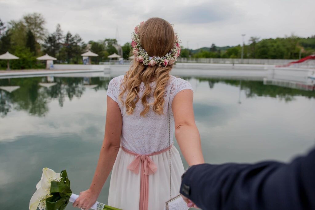 Trauredner Ausbildung online - Braut in weißem Kleid mit Brautstrauß am See von hinten
