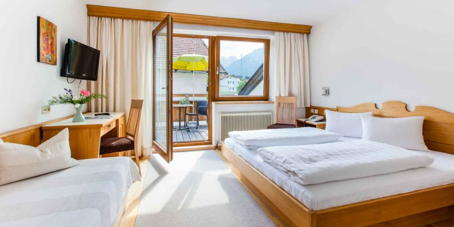 Modernes Hotelzimmer in der Schweiz mit Balkon, zwei Betten, Fernseher und Blick auf die Berge, ideal für Seminar- oder Weiterbildungsaufenthalte.